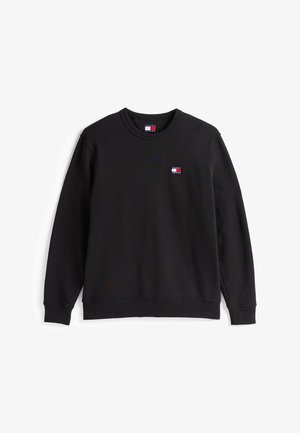 Crna dukserica s rebrastim okruglim izrezom. Ima mali logo s crvenom, bijelom i plavom bojom na lijevoj strani prsnog koša. Mekana tkanina od mješavine pamuka.