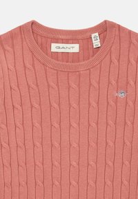 Maglione rosa lavorato a maglia con motivo a treccia, scollo rotondo e un piccolo logo GANT ricamato sul petto.