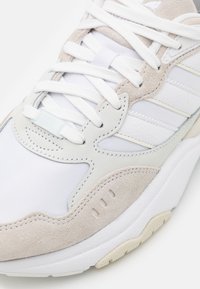 Vit och beige sneaker med rundad form, bestående av mesh- och mockamaterial. Har snörning, diagonala ränder och texturerad sula.