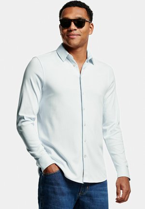 Chemise à manches longues bleu clair avec un col pointu, texture douce et coupe ajustée, associée à un jean en denim bleu foncé.
