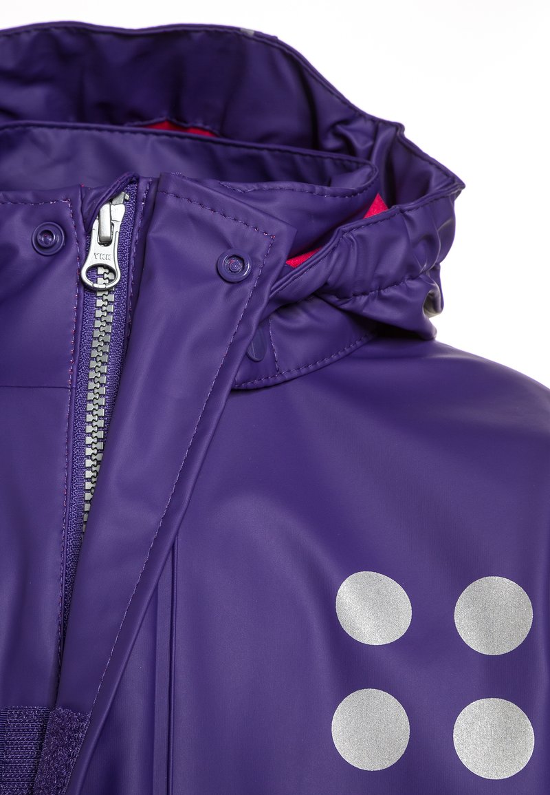 Lila wasserdichte Jacke mit einem Reißverschluss vorne, einer Kapuze und reflektierenden silbernen runden Akzenten auf der linken Seite. Futter in Rot.