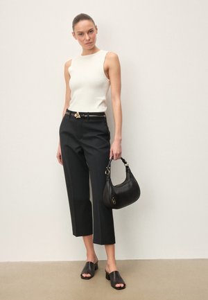 Moteris dėvi baltą berankovį viršutinį drabužį, juodas trumpintas kelnes, juodą diržą su auksine sagtimi, juodus aukštakulnius šlepečius, laiko juodą rankinę.