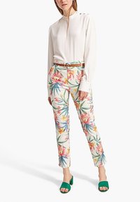 Witte blouse met lange mouwen en knopen, bloemenpatroon broek in pastelkleuren, en groene open teen sandalen met een blokhak.
