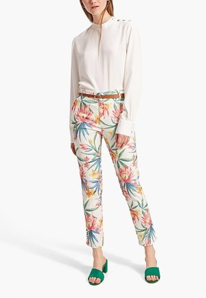 Witte blouse met lange mouwen en knopen, bloemenpatroon broek in pastelkleuren, en groene open teen sandalen met een blokhak.