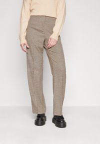 Pantalon à carreaux marron et beige, taille haute, coupe ajustée, poches latérales, porté avec des chaussures à plateforme noires et un pull léger.