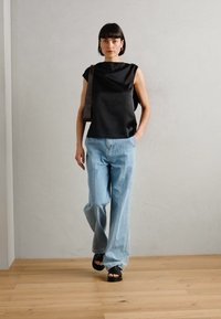 Top in satin nero con maniche corte e colletto alto; jeans azzurri a gamba larga; sandali neri open-toe; design minimalista su uno sfondo neutro.