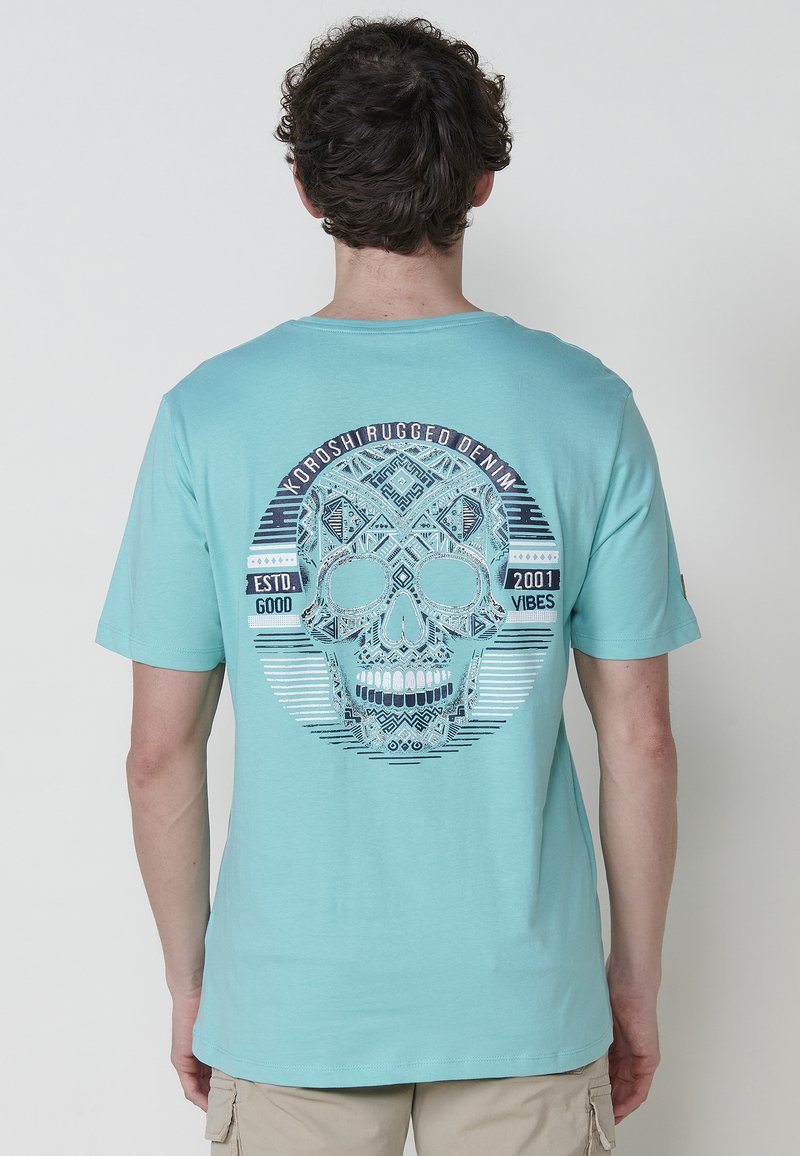 Türkises Baumwoll-T-Shirt mit einem großen Totenkopf-Design, das mit aufwendigen Mustern und Text verziert ist. Kurze Ärmel und ein Rundhalsausschnitt.