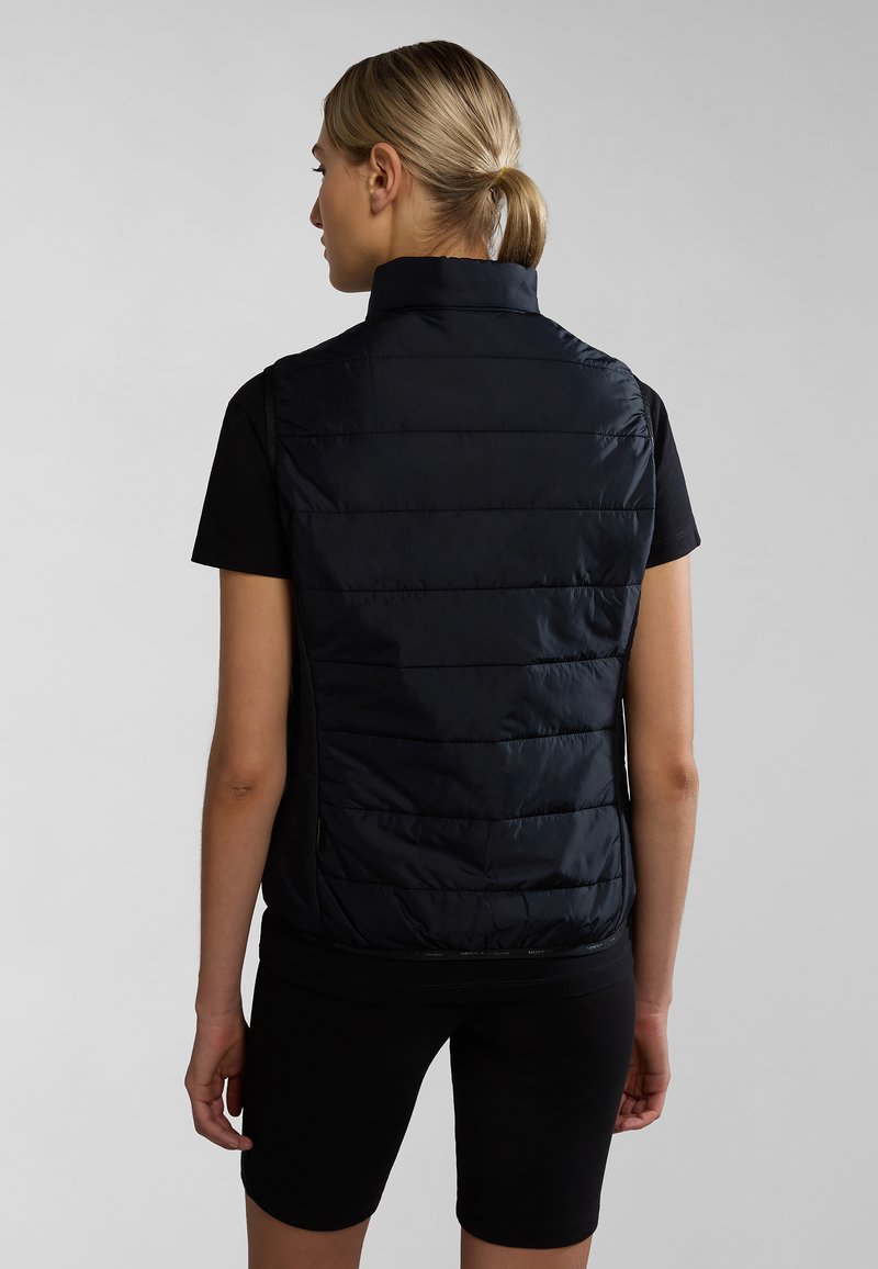 Czarna kamizelka puchowa z pionowym przeszyciem, wysoki kołnierz i kieszeniami bocznymi, zestawiona z dopasowaną czarną koszulą z krótkim rękawem i czarnymi szortami.