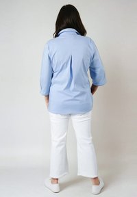 Chemise bleu clair à manches trois-quarts avec pli dans le dos, associée à un pantalon court blanc et des baskets blanches.