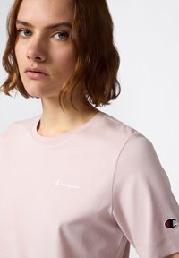 T-shirt in cotone rosa chiaro con scollatura rotonda, che presenta un logo bianco "Champion" sul petto e un piccolo logo ricamato sulla manica.