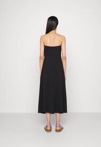 Svart midiklänning utan axelband med en figursydd bodice och flödande kjol. Matchad med lila sandaler som har ankelremmar och en brun sula.