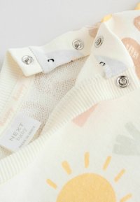 Fehér baba ruhadarab gallér fém patentokkal. Színes nap- és absztrakt mintákkal díszítve. Puha tapintású; pamutból készült. A címke "NEXT baby" feliratot tartalmaz.