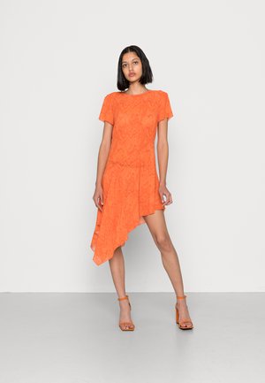 Vestido laranja assimétrico com mangas curtas, tecido texturizado, bainha fluida e combinado com sandálias de salto laranja a condizer.