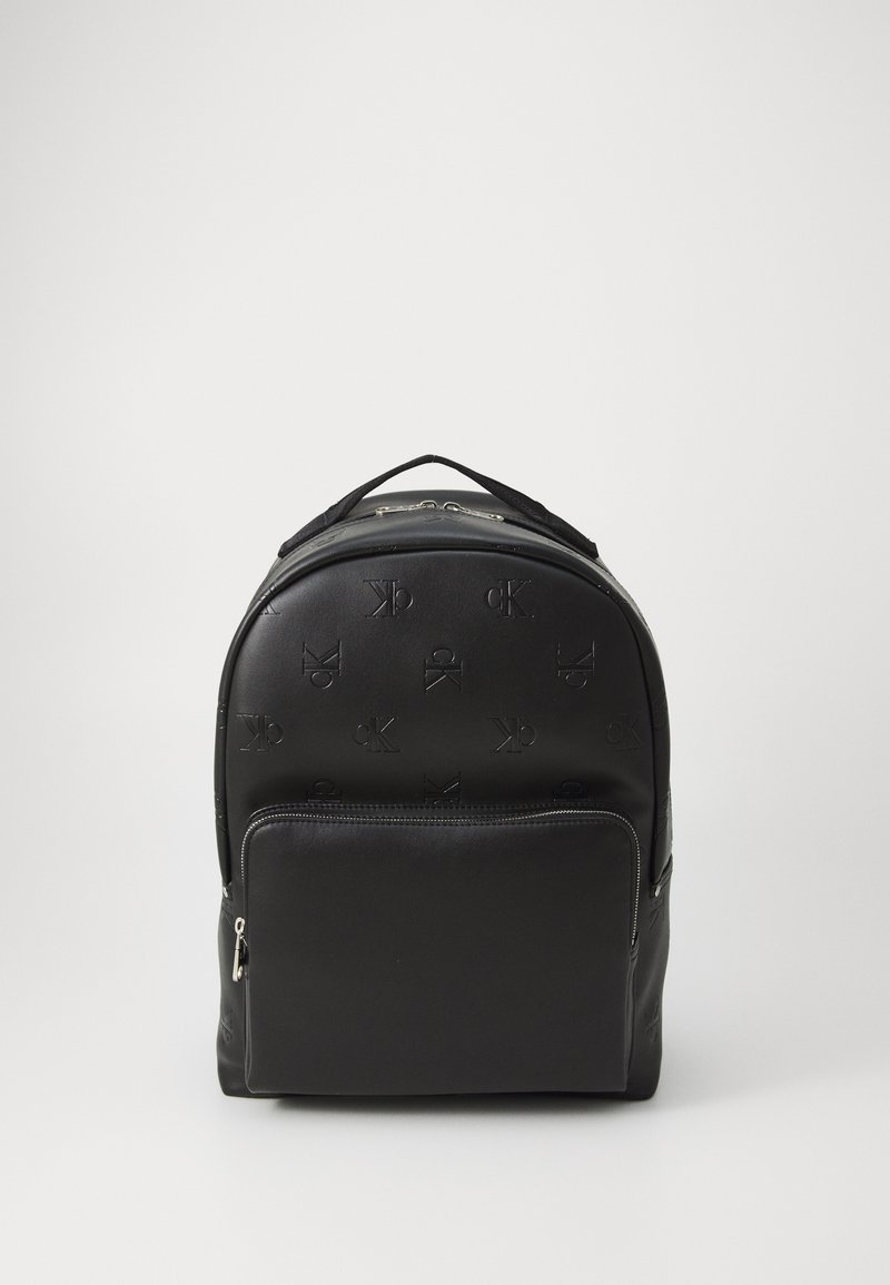Zaino nero realizzato in materiale sintetico testurizzato, con loghi in rilievo, una tasca frontale con zip e una maniglia superiore per il trasporto.