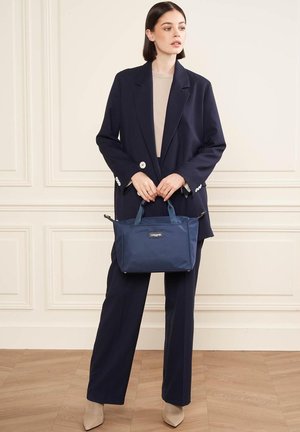 Sac à main bleu marine avec doubles poignées, fabriqué en tissu lisse. Présente un petit logo à l'avant et une forme rectangulaire.