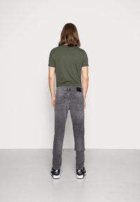 Jeans de mezclilla gris con pierna cónica, con bolsillos traseros y una parcha de logo negra. Combinados con una camiseta ajustada verde y zapatillas negras.