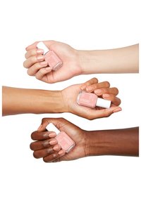 Trois mains tiennent une bouteille de vernis à ongles Essie. Les deux teintes de rose clair et une teinte de rose plus foncé présentent des finitions lisses et des ongles soignés.