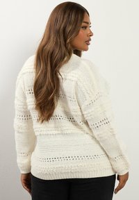 Kremowy, oversize'owy sweter z fakturowanymi paskami i prążkowanymi mankietami. Wykonany z miękkiego dzianiny, zapewnia luźny krój dla wygody.