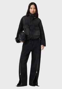 Veste en denim noir avec col montant, deux poches avant et ourlet élastique. Jean large noir assorti avec fermetures éclair dorées sur les côtés.