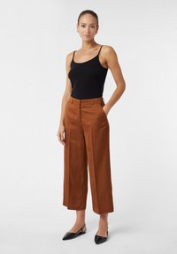 Pantalons marron à jambes larges en tissu lisse, avec une taille plate, des passants de ceinture et des poches latérales. Associés à un débardeur noir ajusté.