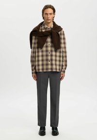 Camisa de cuadros en tonos beige y marrón, combinada con pantalones gris ajustados y un suéter de punto marrón atado alrededor del cuello.