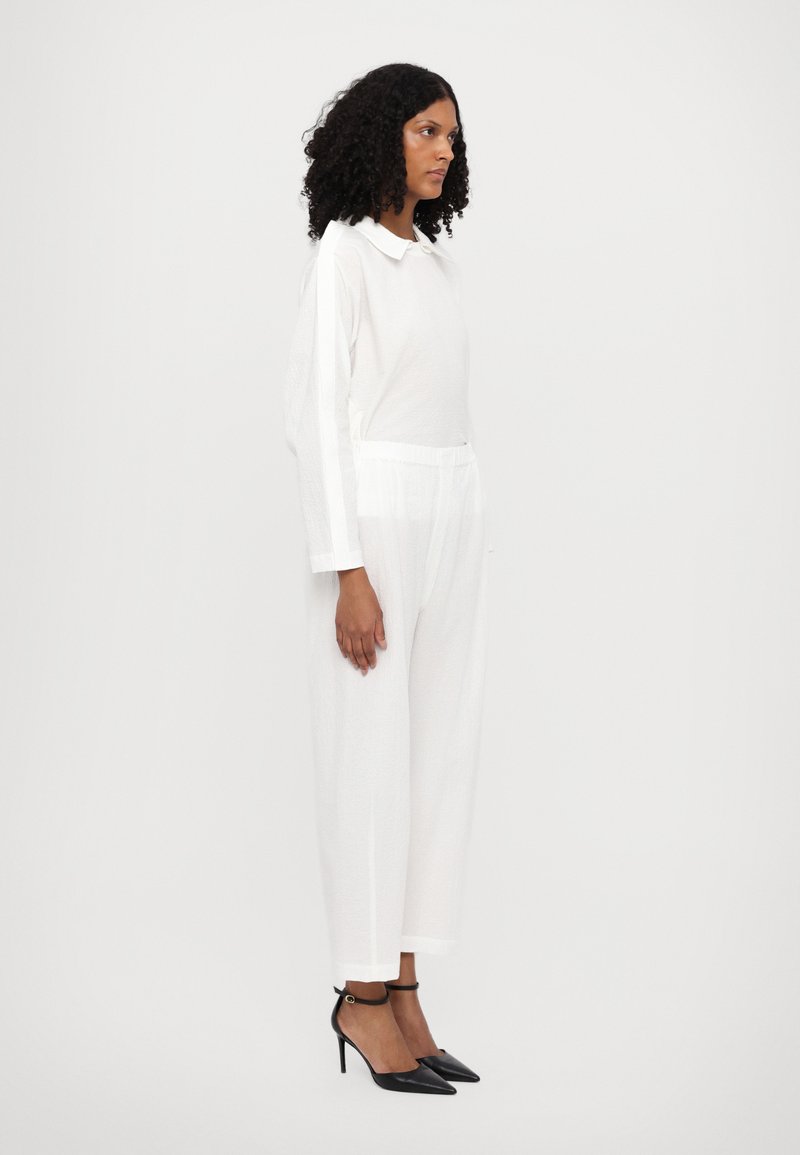 Weißer, langärmliger Pullover-Overall mit Kragen, aus strukturiertem Stoff und mit schmal zulaufenden Beinen. Kombiniert mit schwarzen Stiletto-Absätzen.
