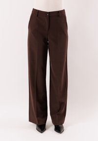 Pantaloni marroni a gamba larga in tessuto liscio, con chiusura a bottone, passanti per cintura e tasche laterali. Indossate scarpe nere con tacco.