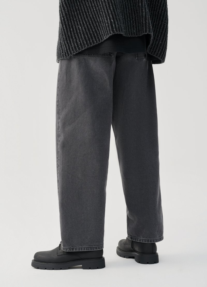 Dunkelgraue Jeanshose mit lockerer Passform, gerade Schnittführung und minimalem Nähen, kombiniert mit schwarzen, klobigen Schnürstiefeln.