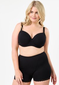 Musta rintaliivi, jossa on pehmustetut kupit ja herttaisesti muotoiltu pitsireunus, yhdistettynä korkeavyötäröisiin mustiin alushousuihin, joissa on samanlainen pitsikoristus helmoissa.