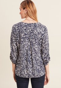 Marinebluse mit weißem Blattmuster, dreiviertelärmel und Rundhalsausschnitt. Weicher Stoff mit lockerer Passform und leicht abgerundetem Saum.