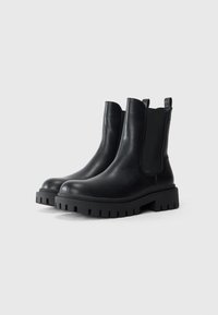 Botas Chelsea de cuero negro con paneles laterales elásticos, punteras redondeadas y suelas de goma gruesa con profundos grabados para mejorar la tracción.