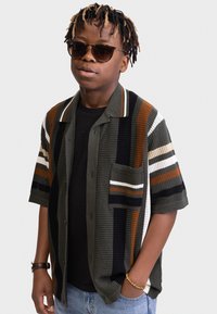 Short-sleeved, multicolored knit shirt featuring dark green, orange, and white stripes; paired with a black t-shirt and sunglasses.