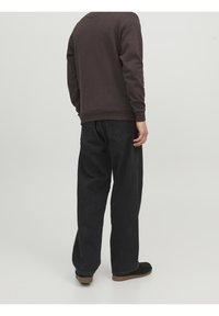 Felpa grigia scura con maniche lunghe, polsini e orlo a coste. Abbinata a jeans neri larghi e scarpe nere slip-on.