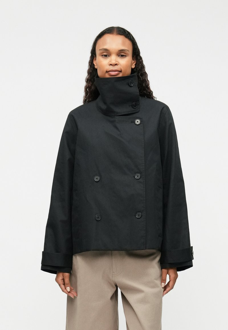 Chaqueta corta negra con un collar alto, botones de doble botonadura y mangas amplias. Confeccionada con una tela suave y ligera.