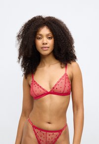 Κόκκινο διάφανο σετ εσωρούχων που περιλαμβάνει σουτιέν σε σχήμα τριγώνου και αντίστοιχο thong. Το ύφασμα περιλαμβάνει κεντημένα σχέδια καρδιάς και λεπτές δαντελένιες πτυχές.