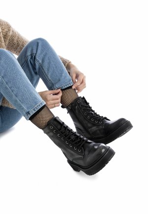Botas negras hasta el tobillo con cordones en el frente y cremallera lateral, cuero texturizado, suelas de goma y tacón grueso. Calcetines de red visibles sobre la bota.