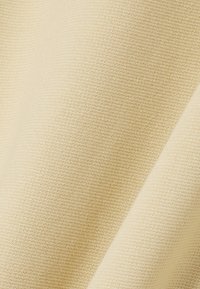 Tissu beige clair avec une surface lisse et texturée. Le matériau présente un motif en tricot fin, mettant en valeur sa douceur et sa flexibilité.