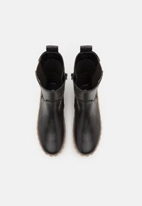 Bottines noires en cuir avec une texture lisse, bout arrondi et semelle en caoutchouc marron. Elles présentent une fermeture éclair sur le côté et un panneau élastique pour un enfilage facile.