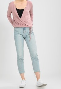 Vaaleanpunainen pitkähihainen kietaisupaita mustan toppauksen päällä, yhdistettynä vaaleansinisiin  cropped-farkkuihin ja valkoisiin lenkkareihin. Farkuissa on revityt helmat.