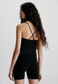 Top nero a costine con spalline incrociate sottili, abbinato a pantaloni corti a vita alta coordinati. Il tessuto ha una finitura testurizzata.