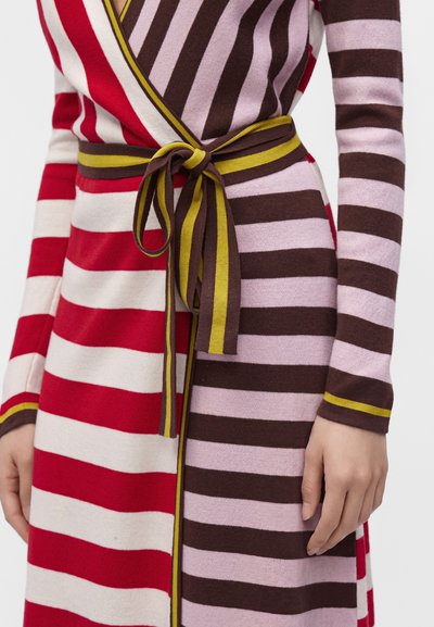 Gros plan d'une robe portefeuille rayée avec des rayures horizontales rouges, crème, marron et roses, nouée à la taille avec une ceinture marron et jaune.