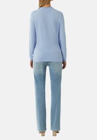 Hellblauer strukturierter Pullover mit langen Ärmeln, rundem Ausschnitt und leicht längerem Rücken. Kombiniert mit hellblauen geraden Jeans.