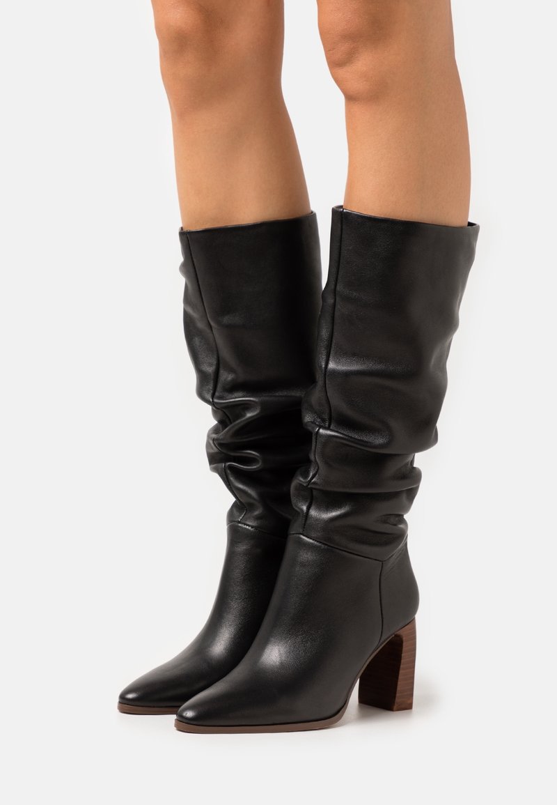 Bottes noires en cuir montant jusqu'aux genoux avec un design froissé, un bout pointu et un talon bloc. Texture lisse avec une finition soignée.