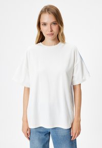 Hvid oversized t-shirt lavet af bomuld. Har korte ærmer og rund hals. Subtile blå sidestropper. Glat tekstur. Casual skæring.