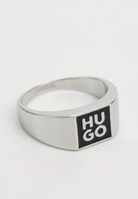 Anello in argento con finitura opaca, caratterizzato da un accento rettangolare nero inciso con il testo "HUGO" in lettering bianco. Bordo liscio.