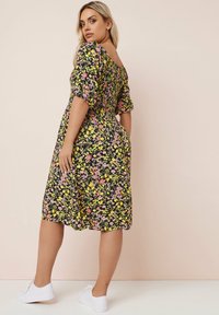 Schwarzes Blumenkleid mit kurzen Puffärmeln, verziert mit gelben und rosa Blumen, tailliert mit einer schmalen Taille und knielanger Länge, kombiniert mit weißen Sneakers.