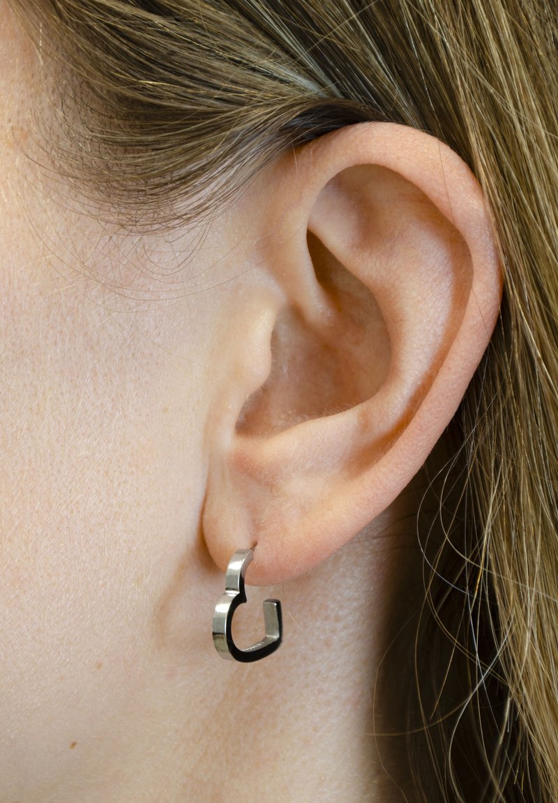 Ohrringe aus silberfarbigem Metall in einer einzigartigen, abstrakten Form. Sie verfügen über eine strukturierte Oberfläche und ein kleines, an der Ohrmuschel befestigtes Hoop-Design.