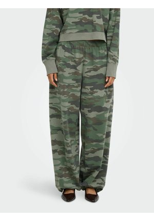 La personne porte un pantalon camouflage ample avec taille élastique et un haut à manches longues assorti, associé à des chaussures pointues foncées.