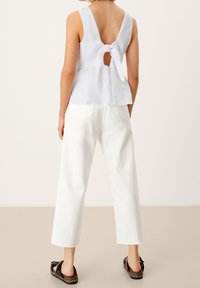 Top bianco senza maniche con dettaglio di laccio sul retro e ritaglio a chiave, abbinato a pantaloni bianchi dritti; sandali piatti con accenti intrecciati.