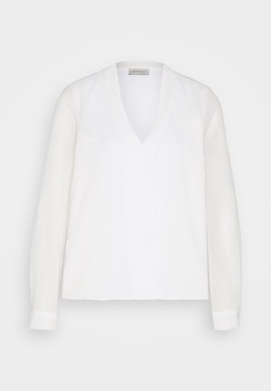 Camicia bianca a maniche lunghe con scollatura a V, caratterizzata da una texture liscia e da dettagli di cucitura frontale sottili, progettata per una vestibilità rilassata.